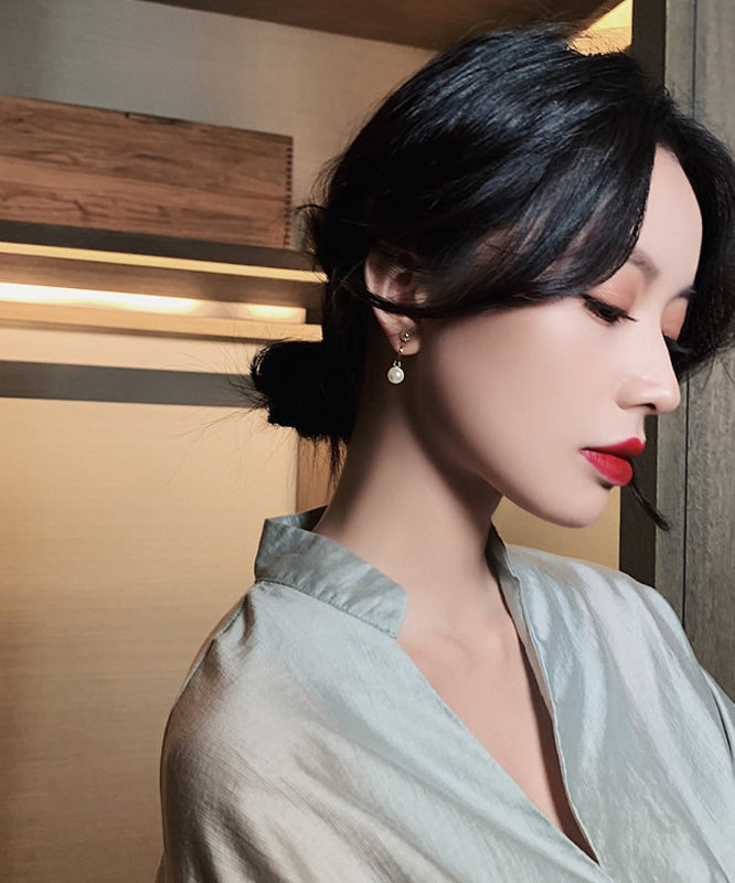 Elegantes pendientes de metal dorado con perla dorada y conexión cruzada